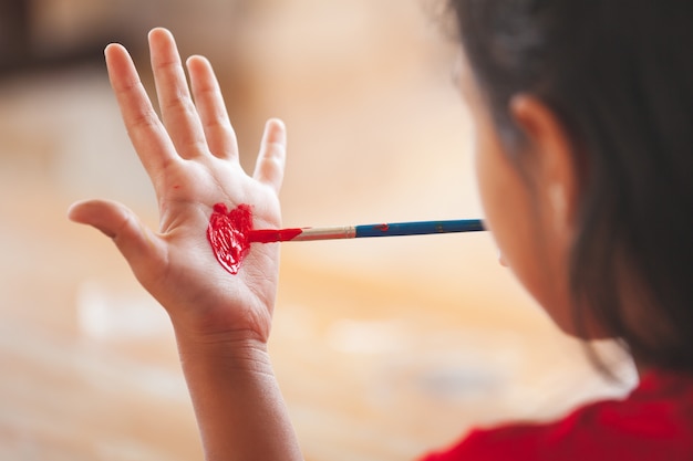 Child drawing and painting a heart on her hand with fun