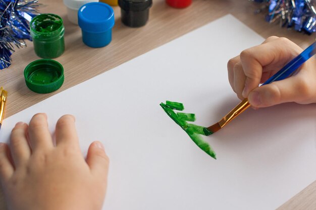 A child draws a Christmas tree Ideas for drawing with bright colors Drawing children on a white background A little girl draws with paint and brushes The concept of children's development