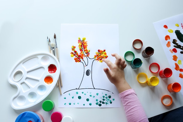 A child draws leafs on a tree Ideas for drawing with finger paints Finger painting for kids on white background Little girl painting by finger hand paint color Children development concept