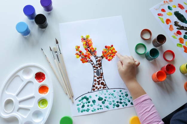 A child draws leafs on a tree Ideas for drawing with finger paints Finger painting for kids on white background Little girl painting by finger hand paint color Children development concept