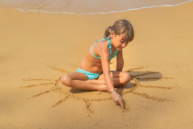 A child draws a sun on the beach.