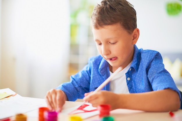 The child draws with a brush watercolor paints on paper the letter A