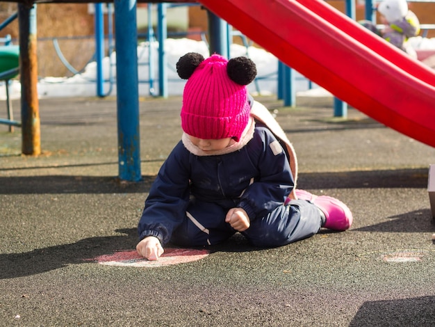 child draws with chalk on the playground on a spring day