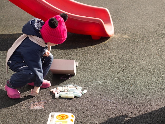 child draws with chalk on the playground on a spring day