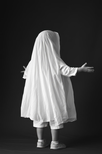 A child dressed as a ghost arms outstretched in a minimalist black and white setting