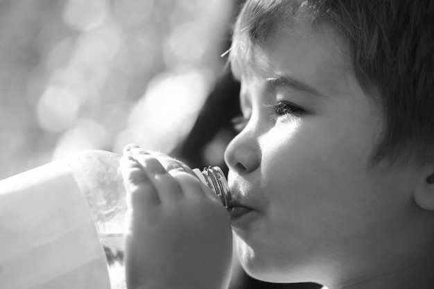 Child drinks water from a bottle while walking, baby health. Boy bottle of water. Young boy holding drink fresh water bottle. Black and white.