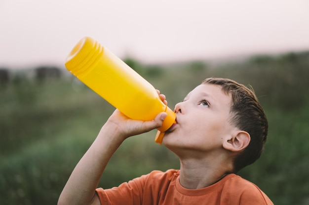 A child drinks water from a orange bottle while walking baby health