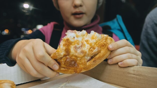 Child eat pizza cheese four Close up of young girl woman eating pizza and chewing in outdoor restaurant Kid children hands taking piece pizza