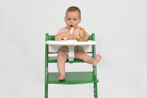 Child eating banana and sitting in a highchair on white background