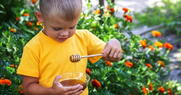 A child eats honey in the garden from a transparent bowl nature