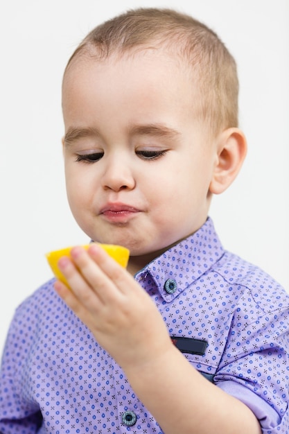 Child eats sour lemon sprinkled with sugar, white background.