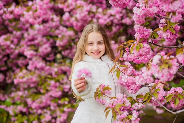 Child enjoy life without allergy Sniffing flowers Girl enjoying floral aroma Pollen allergy concept Kid enjoy cherry blossom sakura Kid on pink flowers sakura tree background Allergy remedy