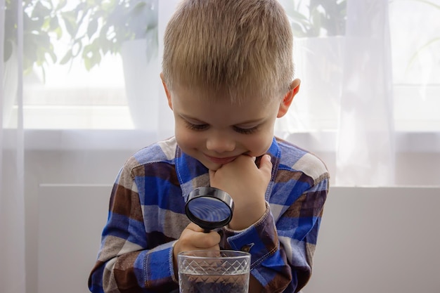 The child examines the water with a magnifying glass in a glass Kid