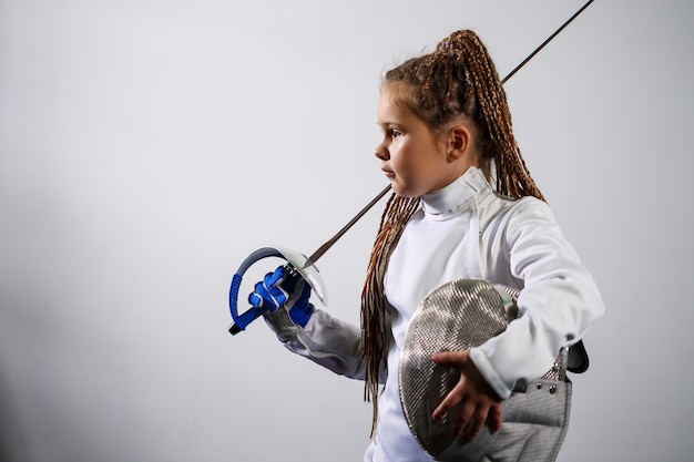 A child in a fencing costume is holding an epee. Girl learning fencing