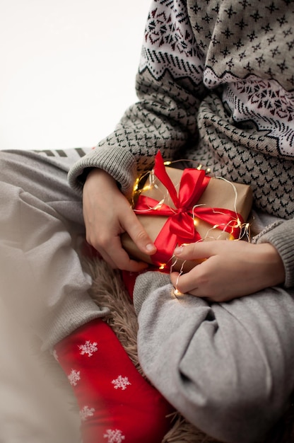 A child in festive clothes holds a gift in craft paper and with a red ribbon in a vertical format