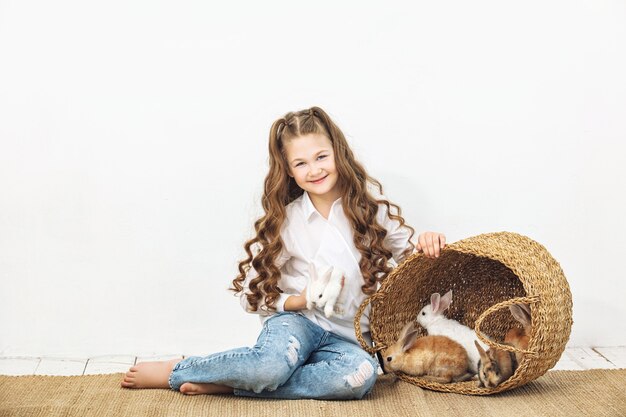 Child girl beautiful cute cheerful and happy with little animals rabbits on white wall background