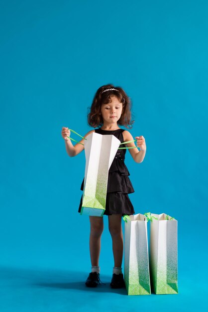 Child girl in a black dress with paper bags on a plain background. Shop for discounts