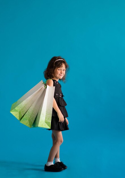 Child girl in a black dress with paper bags on a plain background. Shop for discounts