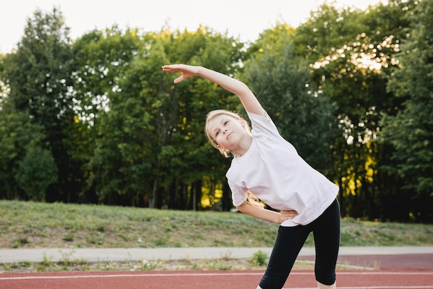 Child girl doing warm up workout outdoor before running on sports track in public park