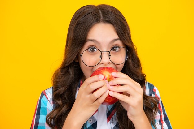 Child girl eating an apple over isolated yellow studio background Close up face of tennager with fruit Portrait of happy funny smiling teenage child girl