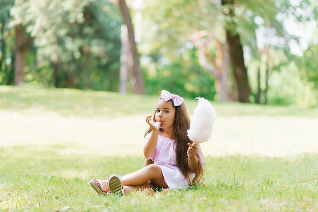 Child girl eats cotton candy on a sunny summer day and licks sticky fingers Walk with children in the park on vacation