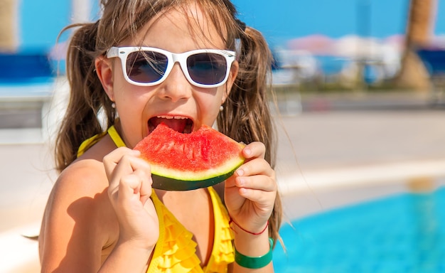 Child girl eats watermelon near the pool