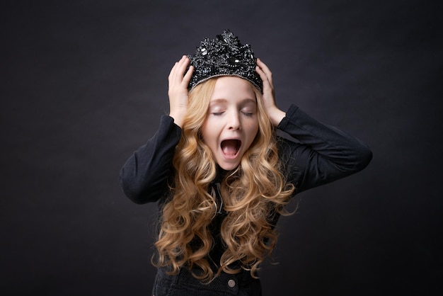 Child girl holding her hands on her head with crown with horror closed her