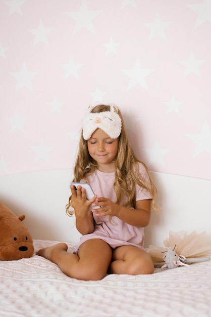 Child girl is sitting on the bed and playing the smartphone