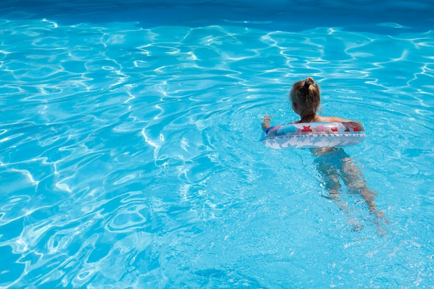 Child girl learn to swim with an inflatable ring in the pool