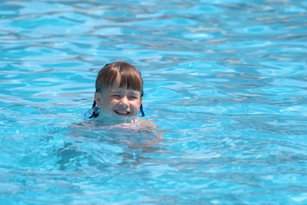 Child girl learns to swim Funny face with closed eyes on bright blue rippled water surface