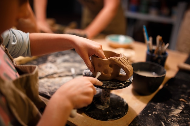 Child girl making a cup from red clay at pottery workshop.