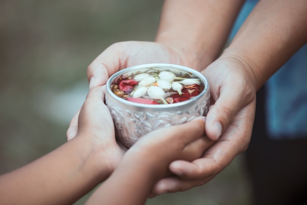 child girl and mother holding bowl that have flower leaf in water for pouring on hands of 