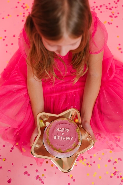 Child girl in a pink dress holds a delicious sweet bento cake with the inscription happy birthday