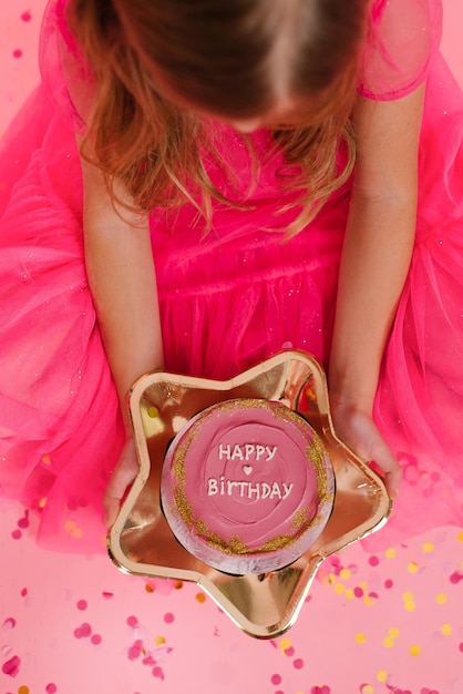 Child girl in a pink dress holds a delicious sweet bento cake with the inscription happy birthday