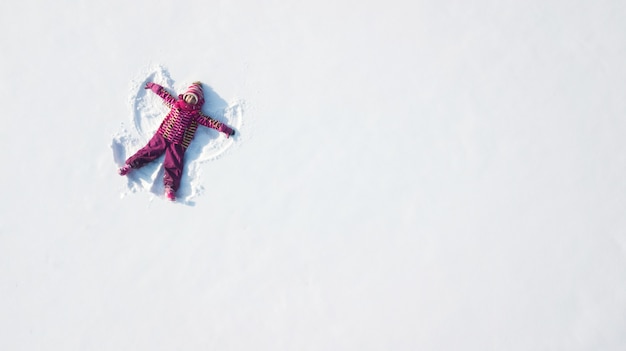 Child girl playing and making a snow angel in the snow. Top flat overhead view