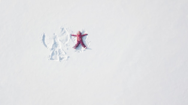 Child girl playing and making a snow angel in the snow. Top flat overhead view