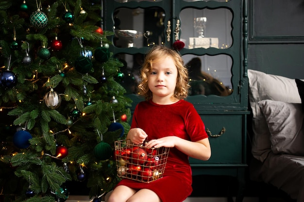 Child girl playing with Christmas decoration near Christmas tree indoors Merry Christmas and Happy Holidays