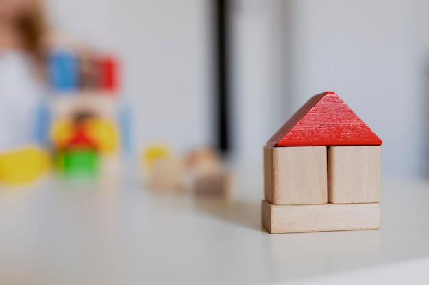 Child girl playing with colorful wooden toy building blocks. Little kid building tower or house at home or day care. Construction block for baby or toddler. Mess in kindergarten play room.