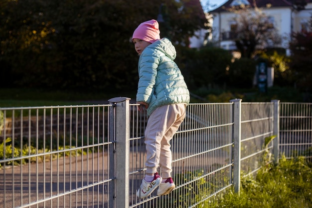 Child girl of preschool age climbs over the iron fence in the park