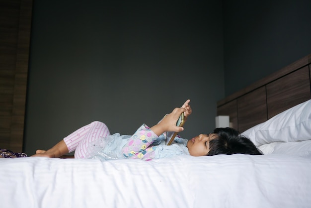 Child girl watching cartoon on smart phone lying on bed