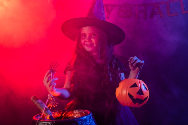 Child girl witch preparing a potion in the cauldron at halloween holidays