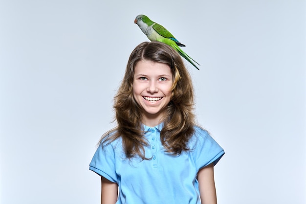 Child girl with pet green quaker parrot looking at camera on light studio background