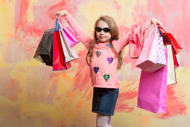 Child girl with present pack on colorful background. Small girl with shopping bag. Christmas and birthday. Holiday celebration and party. Childhood and happiness.