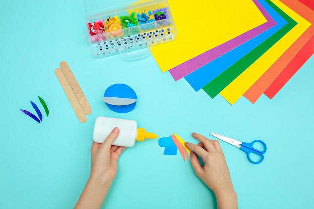 A child glues colored blue paper with glue at the table. Paper crafts for kids.