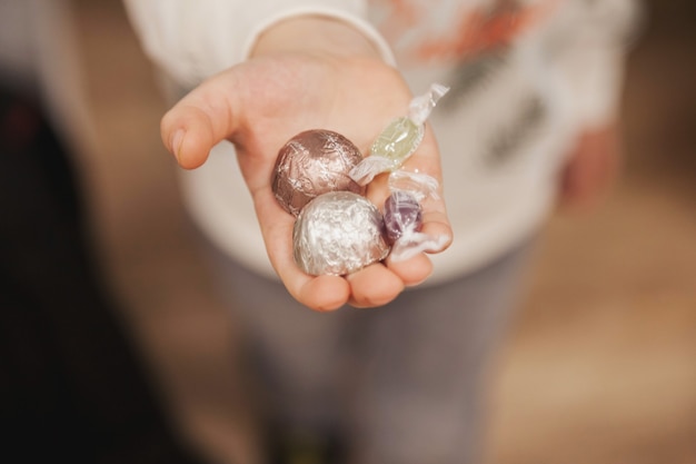 Child hand hold out candy to treat guest. Little boy with colorful sweets in his hands symbolizes cozy comfort and hospitality. Concept of inviting guests and giving gift. Selective focus. Copy space