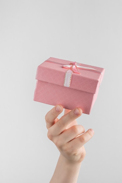 Child hand holding gift box with pink bow white and gray background with copy space