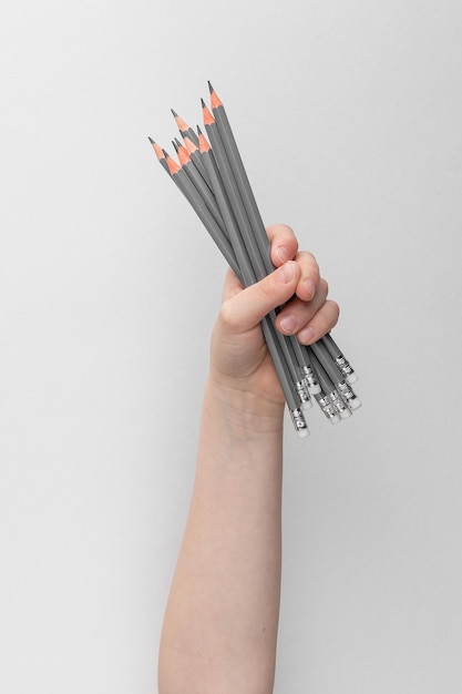 Child hand holding many pencils above a white and gray background copy space