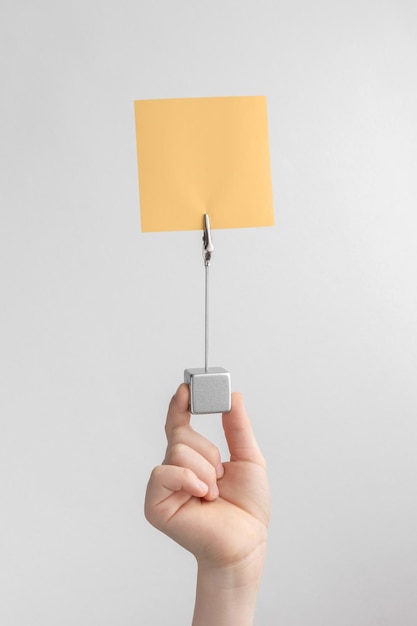 Child hand holding orange blank reminder or paper notes above a white and gray background copy space