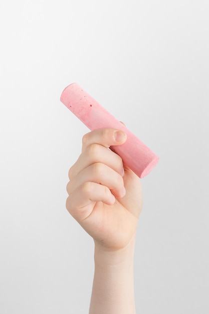 Child hand holding a piece of pink chalk white and gray background with copy space