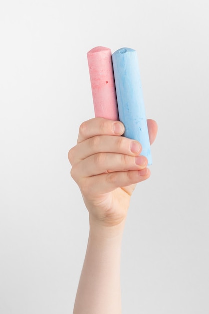 Child hand holding pieces of pink and blue chalk white and gray background with copy space